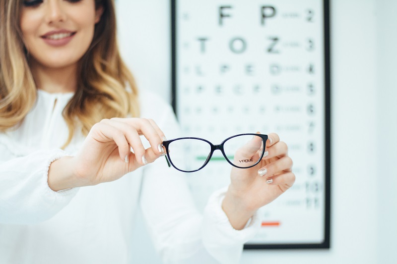 person holding pair of glasses against a vision exam chart
